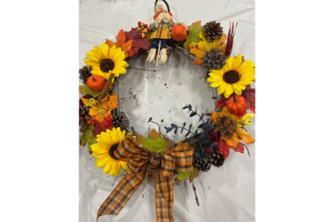 Wreath wit silk flowers in orange, yellow and red with a mini scarecrow at the top.